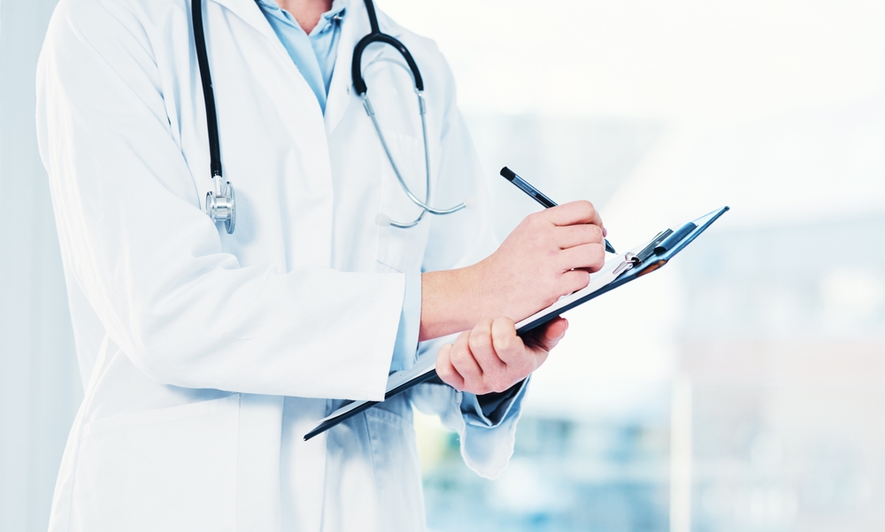 Doctor writing notes on clipboard for newborn's medical costs and treatment plan after Erb’s palsy diagnosis.